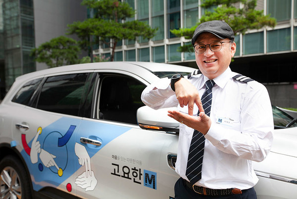 청각장애인 기사님이 수어 아티스트 '지후트리'가 '자립'이라는 수어를 이미지화해 디자인한 '고요한M' 차량 앞에서 '자립'이라는 의미의 수어를 하고 있다.(사진=SK텔레콤)